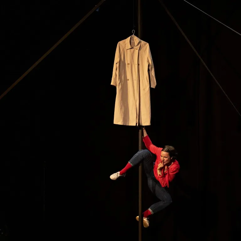 A physical theatre performer suspended beside a coat