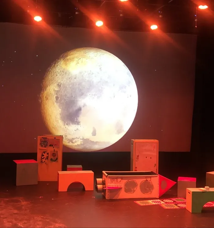 A devised theatre set beneath a projected moon