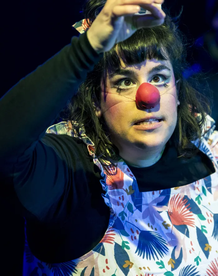 Ruthie in a red clown nose, looking up with one arm raised